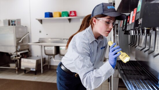 Ecolab expert in restaurant kitchen inspecting soda machine for pests.