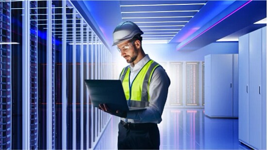 employee in PPO using laptop in front of data center aisle